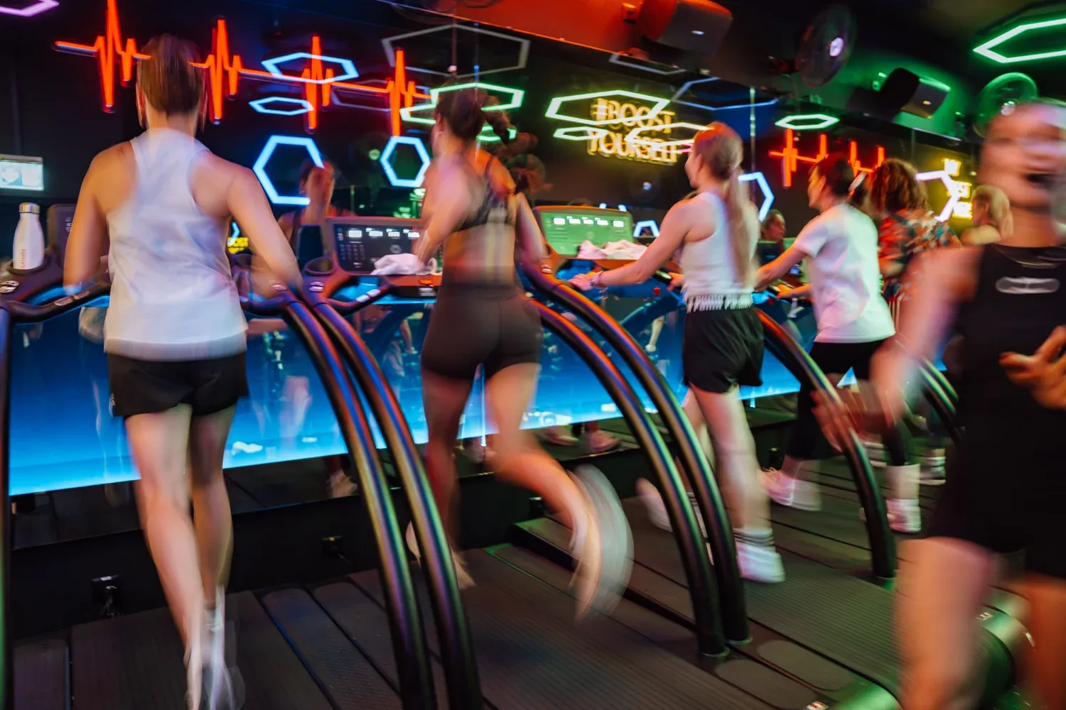 Boosters running on the curved treadmills under the neon of the ReBoost room at CASA BOOST Eaux-Vives