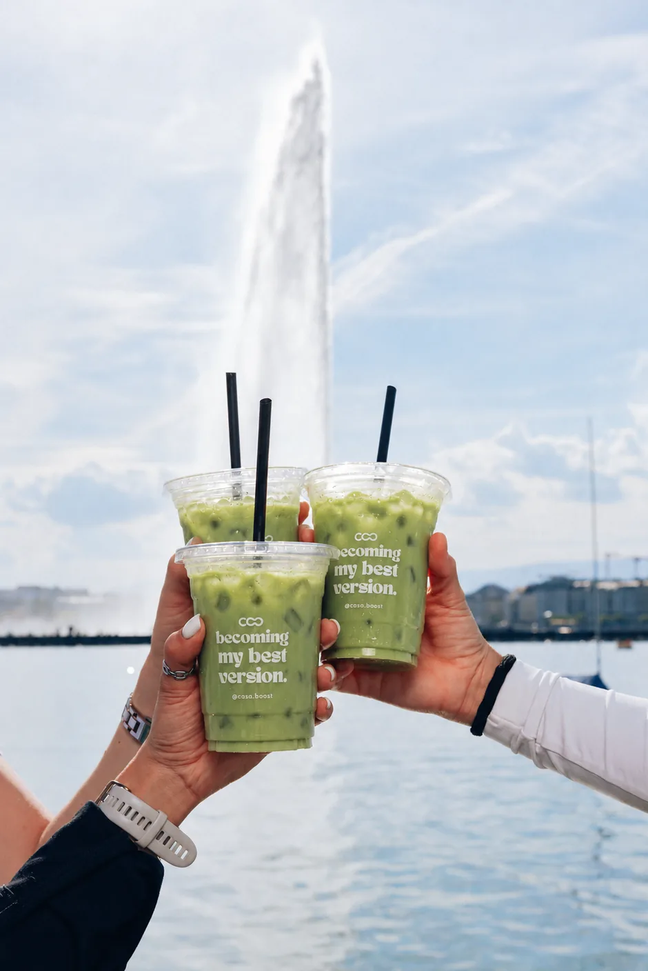Three iced matchas raised in front of the Jet d&rsquo;Eau in Geneva